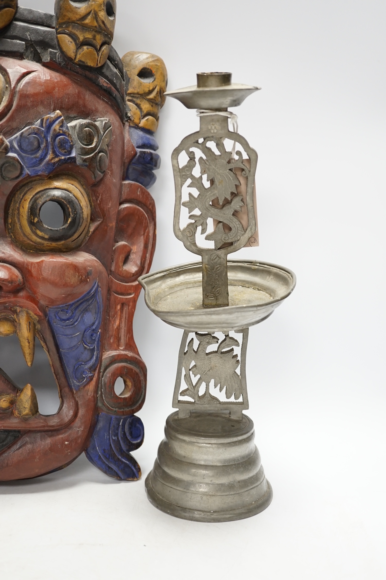 A Tibetan painted wood mask and a cast pewter candlestick, mask 44cm high